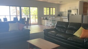 A spacious living area with a black leather sofa, a wooden coffee table, and a kitchen in the background.