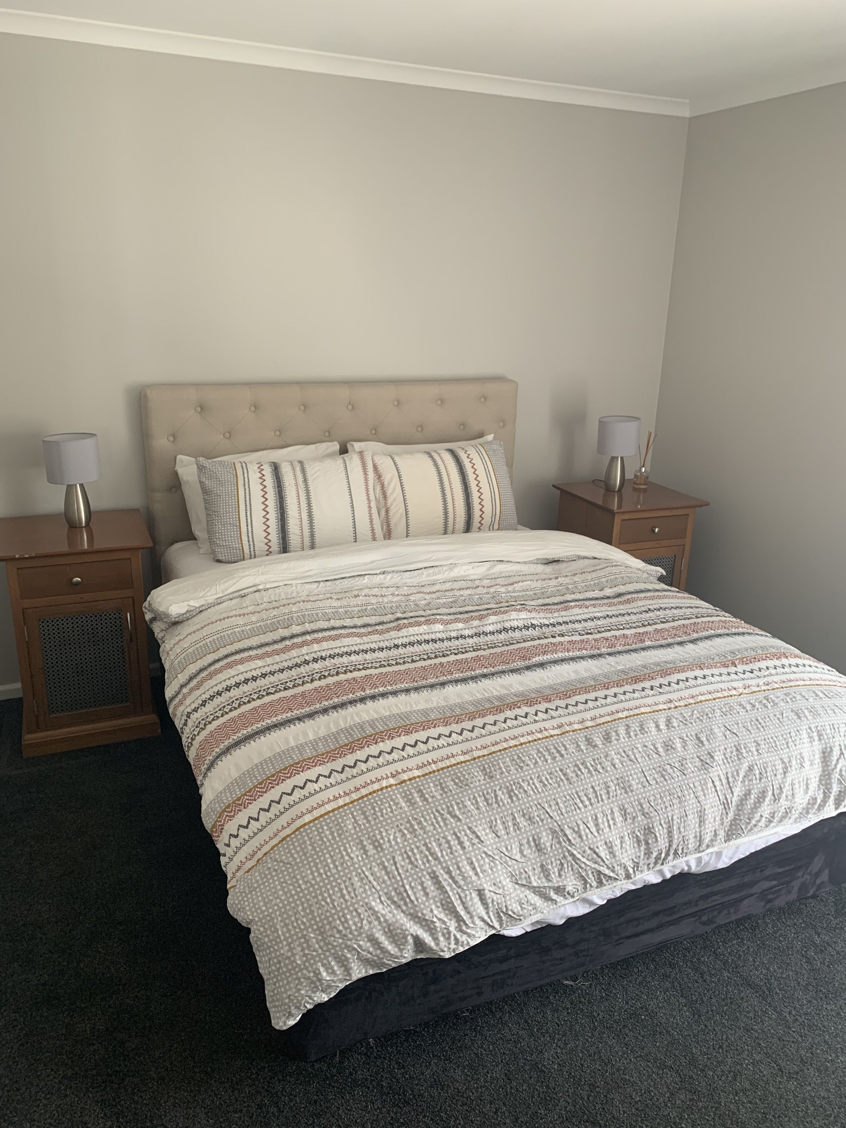 A neatly made bed with a striped bedspread, two bedside tables with lamps, and a dark carpeted floor.