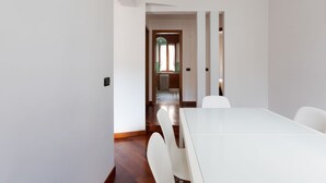 Ein modernes Interieur mit einem weißen Tisch und Stühlen, Holzboden und Blick in einen Küchenbereich.