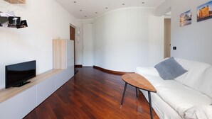 Ein modernes Wohnzimmer mit einem Flachbildfernseher, einem weißen Sofa, einem kleinen Couchtisch aus Holz und einer Holzkassette.