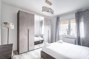 Una habitación de hotel moderna con una cama grande, un armario, un escritorio y una ventana con cortinas.