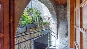 Visão do interior com um arco de pedra, uma porta de madeira e uma varanda com plantas em vasos.