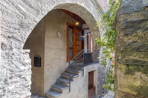 En bygning i sten med dør i træ, trappe og lille balkon med gelænder i metal.
