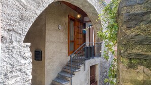 Um edifício de pedra com porta de madeira, escadaria e pequena varanda com grade de metal.