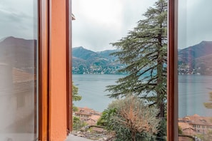 A view through a window of a lake with mountains in the background and a building with a red roof in the foreground.
