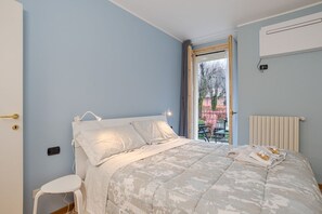 Ein Schlafzimmer mit einem Bett, einem kleinen Hocker, einem Heizkörper und einem Fenster mit Blick ins Freie.