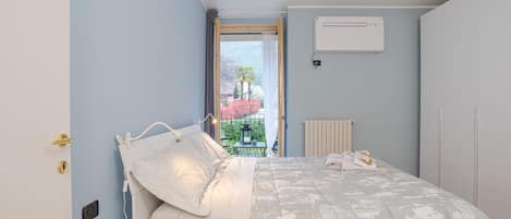 A bedroom with a bed, a radiator, an air conditioning unit, and a view of the outside.