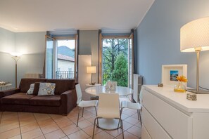 A living room with a brown sofa, white chairs, a round table, and a window with a view of trees and mountains.
