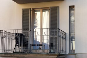 Ein Balkon mit Metallgeländern, ein Fenster mit Rollläden und ein Stuhl.