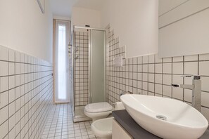 Ein Badezimmer mit einem weißen Waschbecken, zwei Toiletten und einer Dusche.