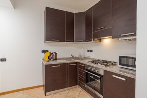 A kitchen with dark cabinets, a gas stove, an oven, and a microwave.