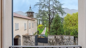 Une vue d’un bâtiment avec un mur en pierre, un portail en métal et un arbre au premier plan.