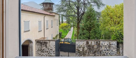 Une vue d’un bâtiment avec un mur en pierre, un portail en métal et un arbre au premier plan.