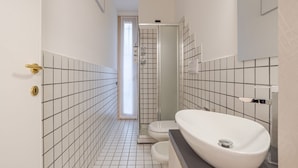 Une salle de bain avec un lavabo, des toilettes et une douche, le tout de couleur blanche.