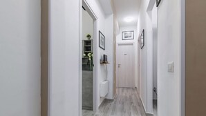 Un pasillo estrecho con piso de color claro, paredes blancas y una puerta al final.