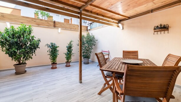 Un patio al aire libre con una mesa y sillas de madera, rodeado de plantas en macetas.