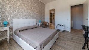 Un dormitorio con cama, mesita de noche, silla, escritorio y puerta que da a otra habitación.