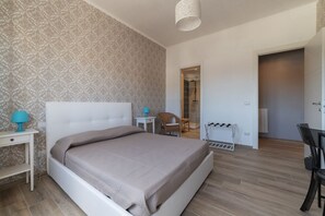Ein Schlafzimmer mit einem Bett, einem Nachttisch, einem Sessel, einem Schreibtisch und einer Tür zu einem anderen Raum.