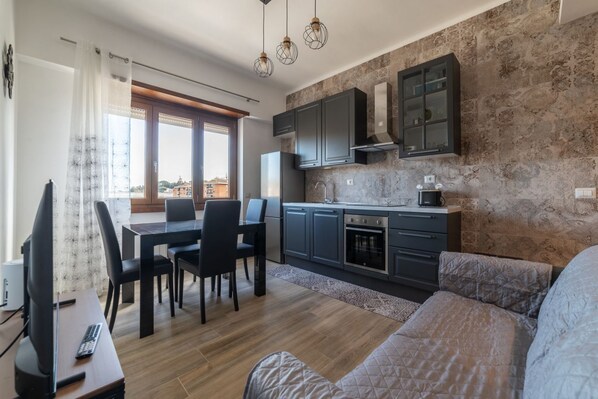 Une cuisine moderne avec des meubles de couleur sombre, un coin repas avec une table et des chaises, et une grande fenêtre.