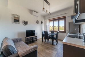 Un salon moderne comprenant un canapé, un téléviseur, une table à manger et des chaises. Il y a également un coin cuisine avec un évier et des placards.