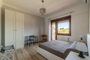 Une chambre à coucher comprenant un lit, un bureau, une chaise, un luminaire suspendu et une fenêtre donnant sur un paysage.