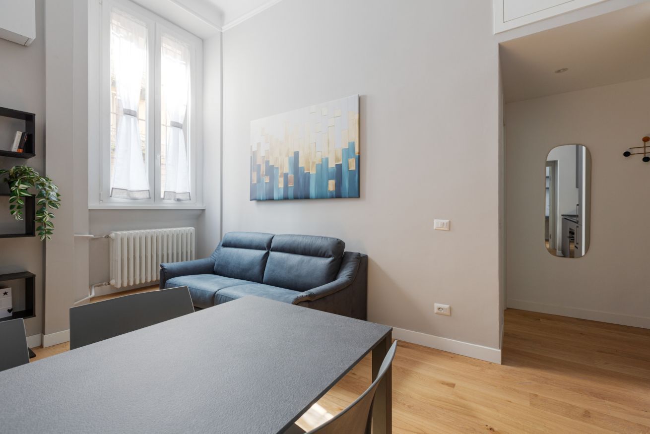 A modern living room with a sofa, a table, a radiator, and a painting on the wall.