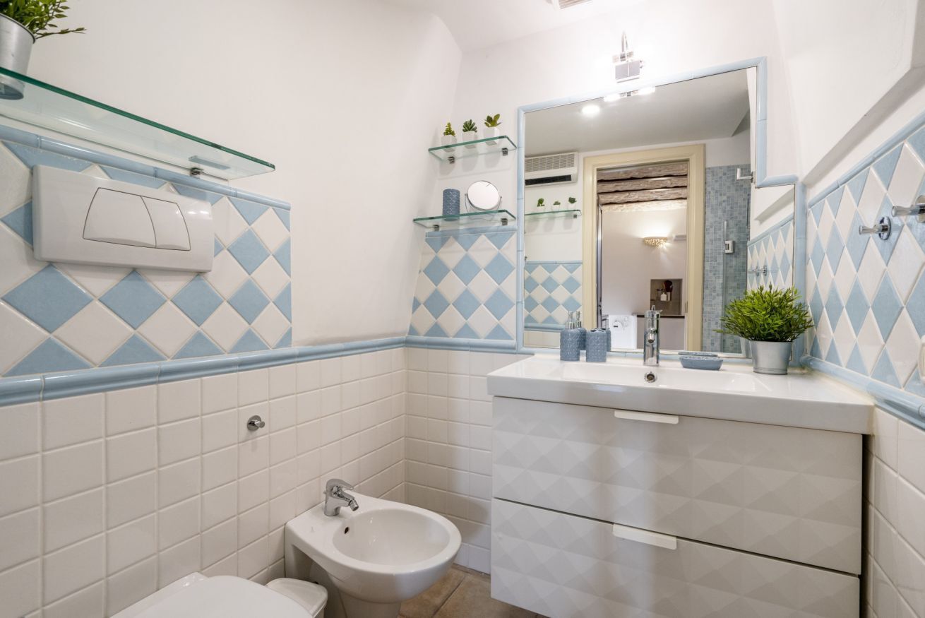 A bathroom with a bidet, a sink with a mirror, and a glass shelf with toiletries.