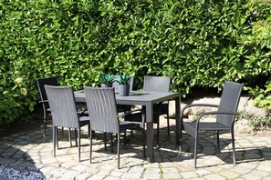 Een terras buiten met een tafel en vier stoelen, omringd door een haag.