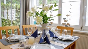 Mesa de comedor para cuatro personas, con platos blancos, vasos y un centro de mesa con flores blancas en un jarrón.