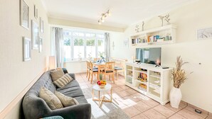 Una sala de estar con sofá, mesa de comedor, sillas, televisor y estantería.