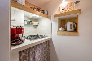 Een keuken met een gasfornuis, een rode koffiezetapparaat en planken met potten en een waterkoker.