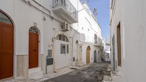 A narrow street with white buildings, wooden doors, and stone paving. - GuestHost - White Lotus Apartment (Ostuni)
