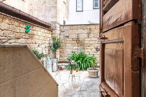 Une cour bordée de murs en pierre, avec une porte en bois et des meubles d’extérieur.