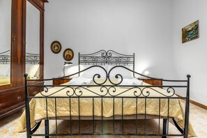 Een bed met een metalen frame, een houten garderobe en een spiegel.