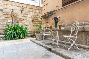 Een terras met een stenen muur, metalen stoelen, een tafel en plantenpotten.