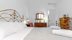 Un lit bien fait, avec une tête de lit, une commode en bois, un miroir et une lampe.