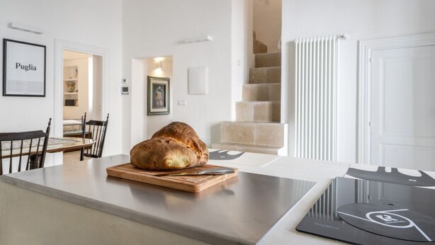A kitchen with a loaf of bread on a cutting board, a digital scale, and a framed picture on the wall. - GuestHost - Before Sunset Appealing Apartment with Terrace (Ostuni)