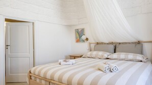 A bedroom with a bed, a bedside table, a nightstand, a door, and a wall-mounted light fixture. - GuestHost - Before Sunset Appealing Apartment with Terrace (Ostuni)
