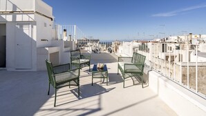 A rooftop terrace with a white building, green metal chairs, a small table, and a view of the sea. - GuestHost - Before Sunset Appealing Apartment with Terrace (Ostuni)