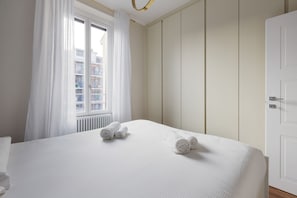 A hotel room with a bed, a window with curtains, a radiator, and a door.