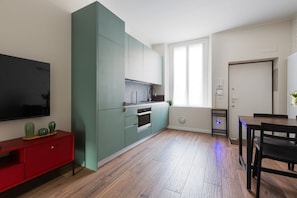 Een moderne keuken met blauwgroene kastjes, een rode console en een eethoek met een houten tafel en stoelen.
