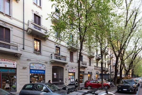 A street view with multi-story buildings, parked cars, and trees.