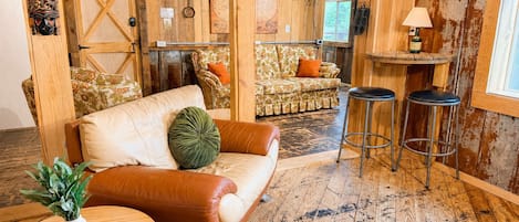 A rustic interior with a leather sofa, a round wooden table, and a bar area.