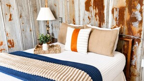 A bed with a blue and beige blanket, a white lamp, and two pillows with beige and orange stripes.