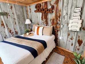 Un dormitorio con cama, almohadas, una lámpara, un toallero de pared y una pared rústica.