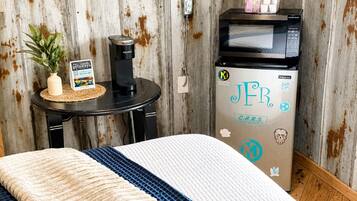 A room with a bed, a small table with a Keurig coffee maker, a microwave, and a refrigerator with stickers.