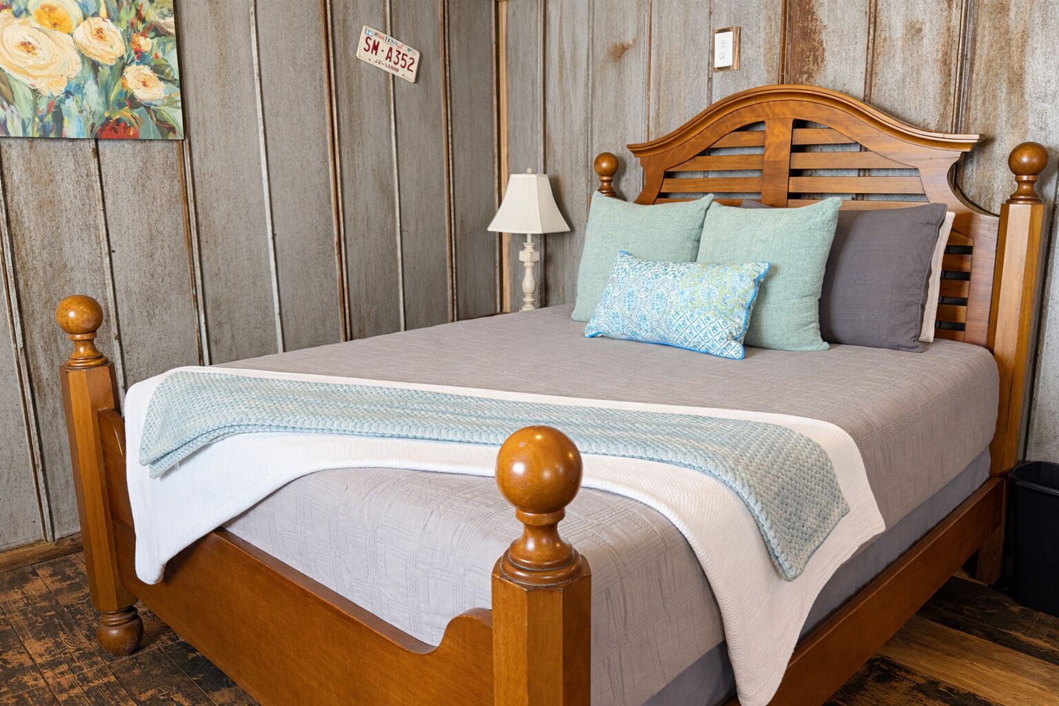 A wooden bed with a headboard, a bedside lamp, and a floral painting on the wall.