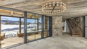 A spacious room with large windows offering a view of a snowy mountain landscape. A wooden staircase leads to an upper level. - Telluride Ranch / Mountain Views, Hot Tub & Fire Pit (Placerville)