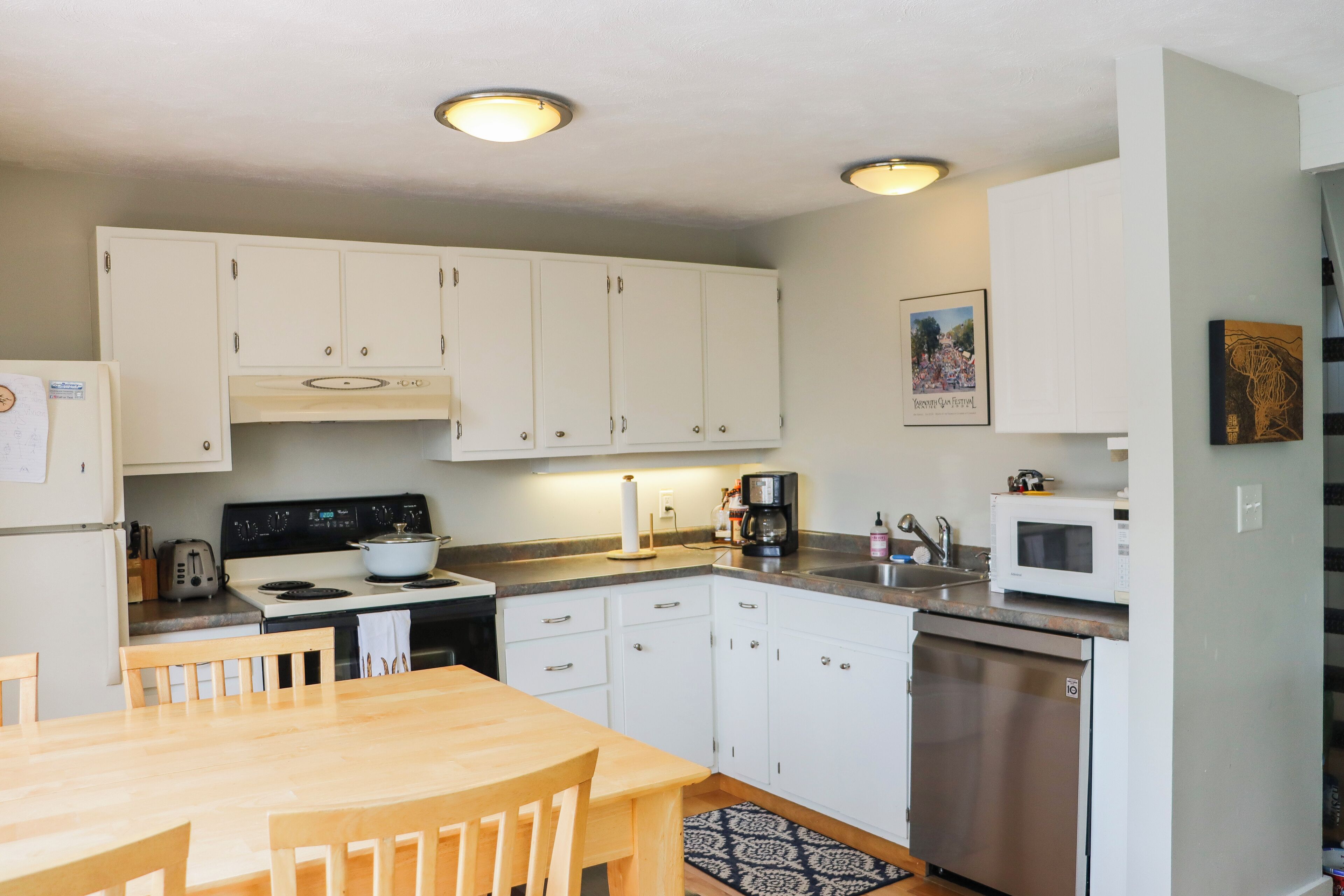 A compact kitchen with white cabinets, a wooden dining table, and basic appliances including a stove, microwave, and dishwasher.