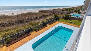 A swimming pool with a wooden deck, a beach view, and a poolside lounge area. - Windy Shores-Oceanfront 2BD Condo-Pool-Pet Friendly (North Myrtle Beach)